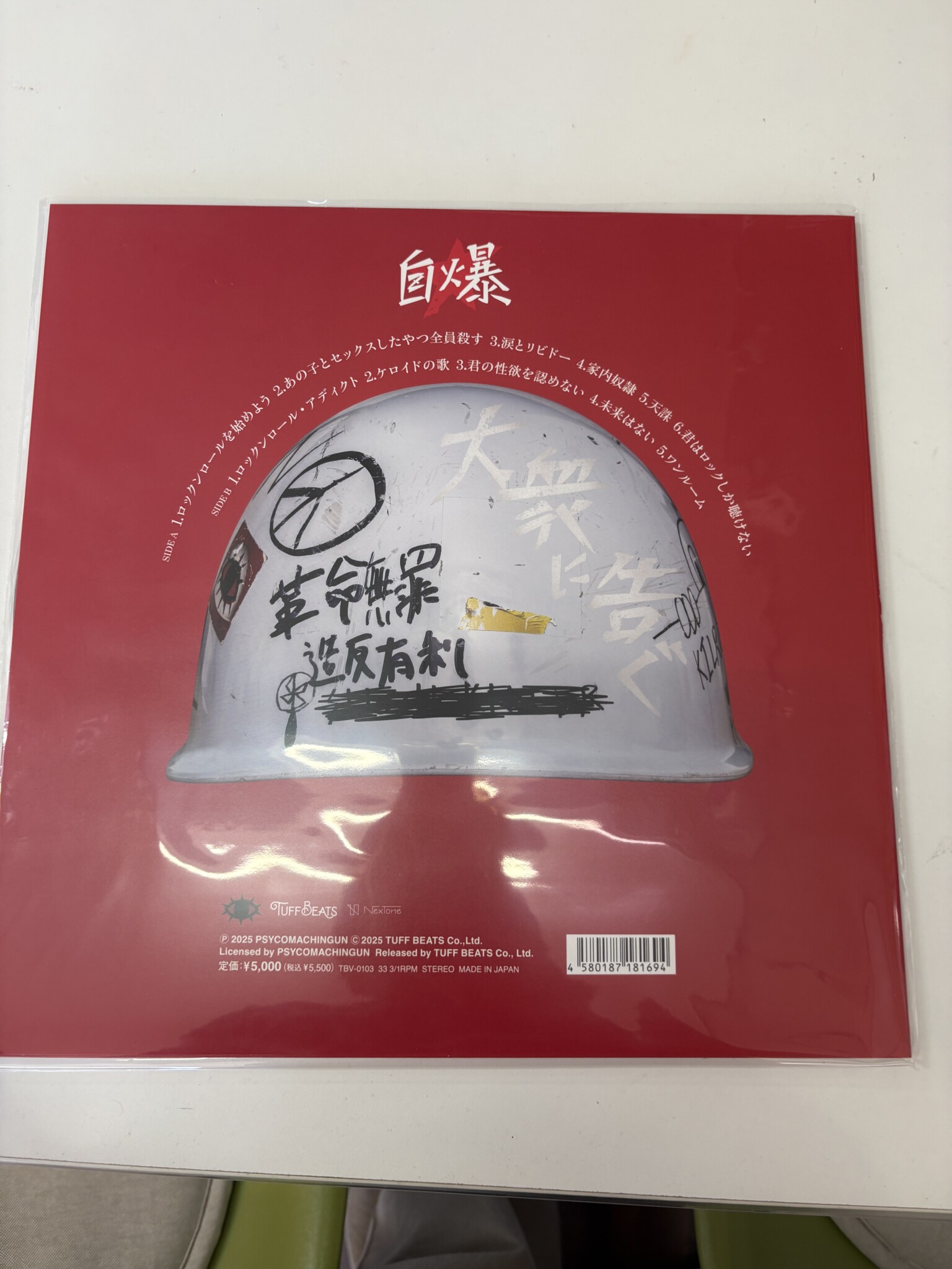 自爆「大衆に告ぐ」のレコードジャケット裏面。落書きだらけのヘルメットのまわりに曲名が並ぶ。