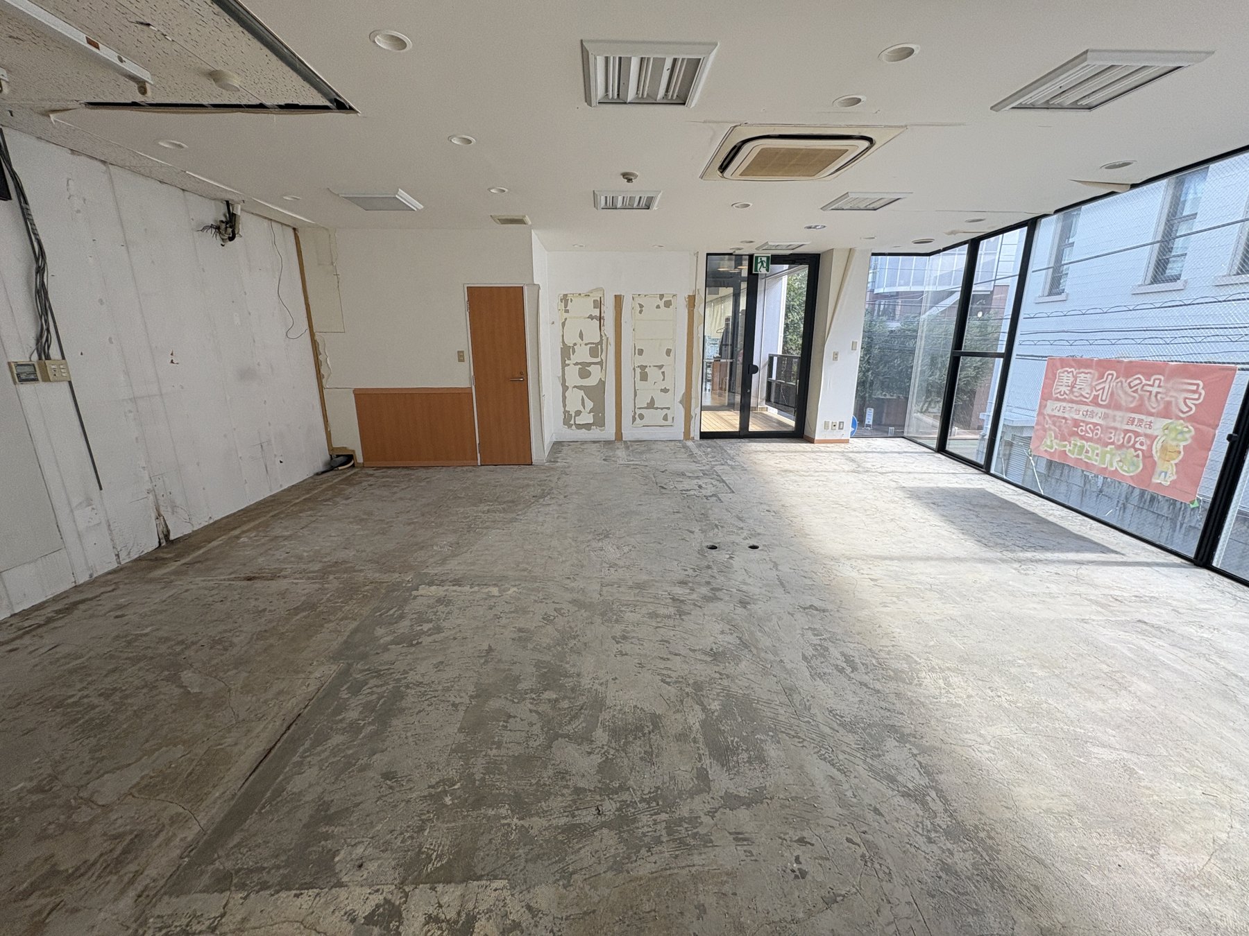 2-Aの現況。大きなガラス面、空室の床と壁、右奥の入口が見える室内写真