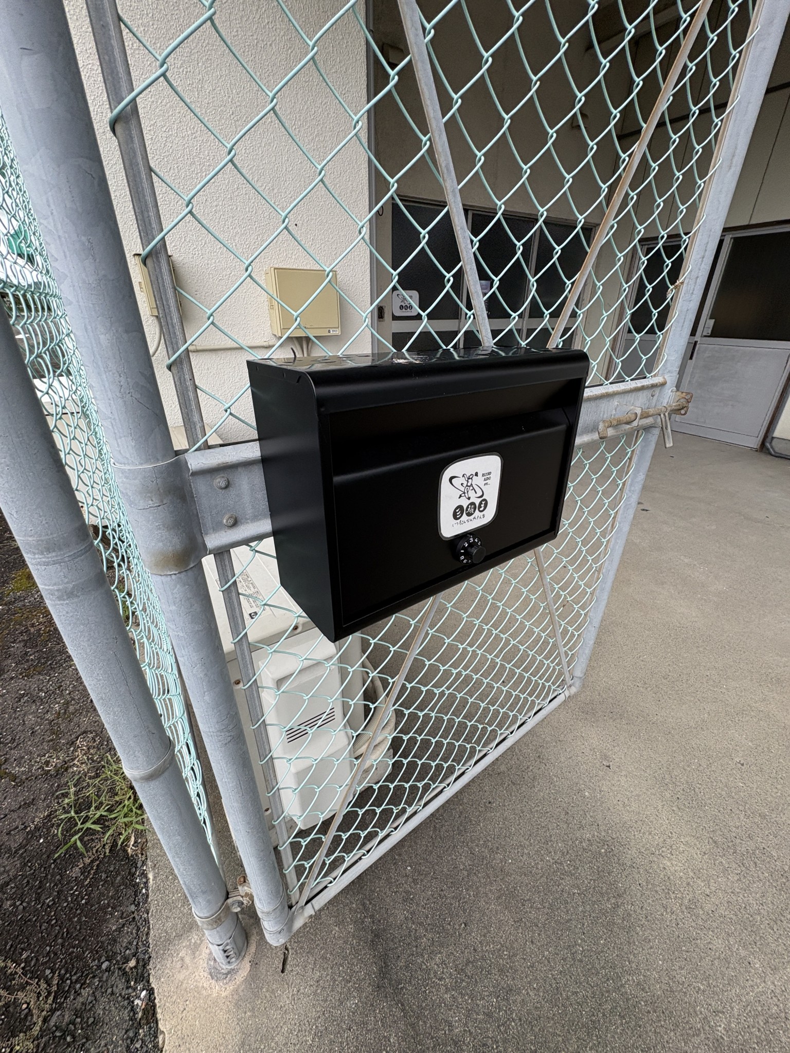 金網の門扉に設置された黒い郵便ポスト